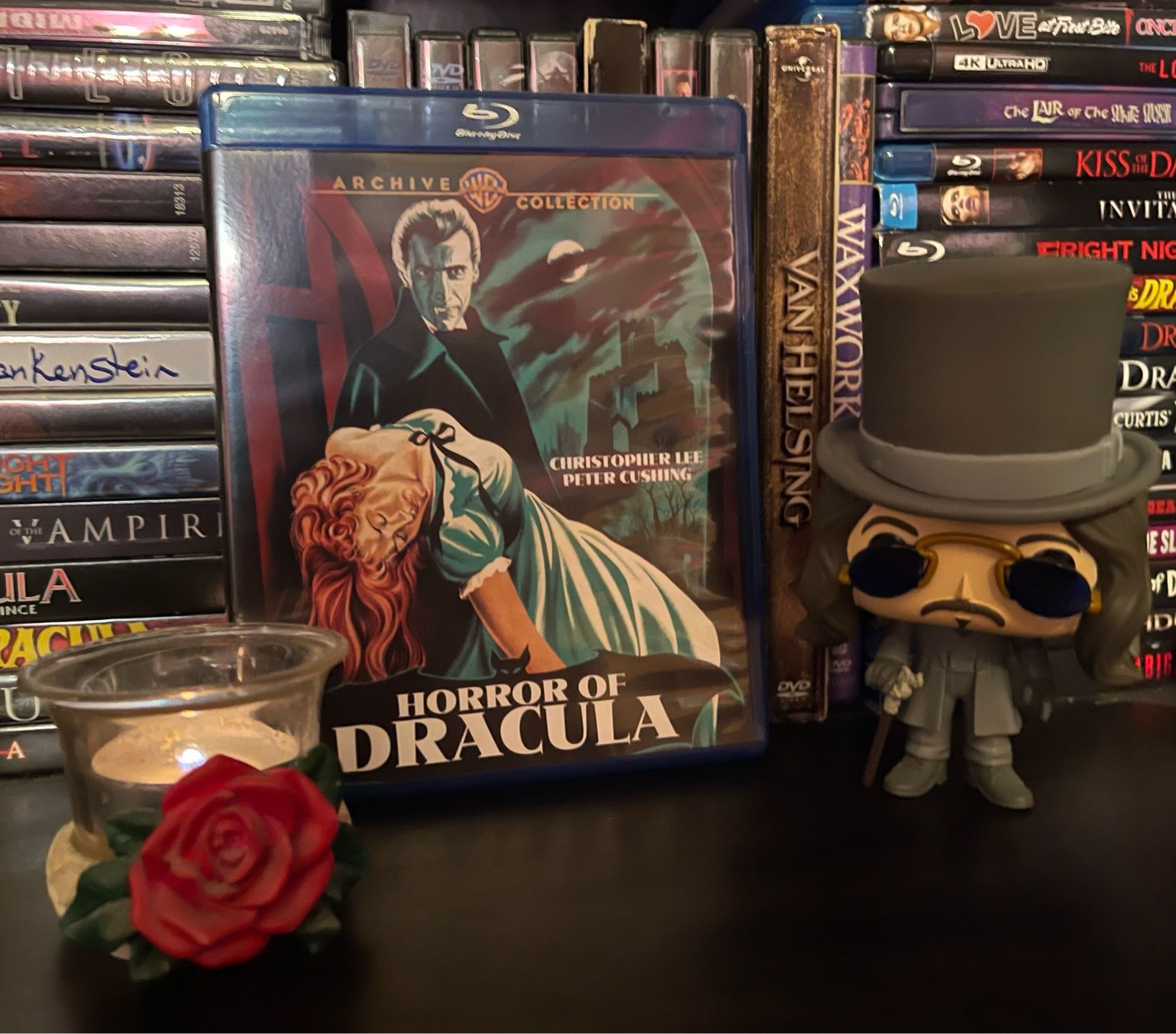 A movie shelf featuring a blu ray of The Horror of Dracula, framed by a Gary Oldman Dracula Funko Pop and a rose candle holder with a tiny tea light inside it.